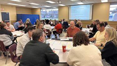 Group of students and staff collaborate at round tables