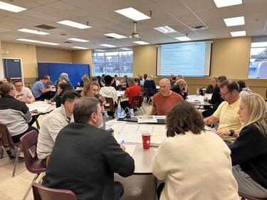 Group of students and staff collaborate at round tables
