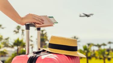 iStock Image - Travel Woman with pink suitcase and passport with boarding pass standing on passengers ladder of airplane opposite sea with palm trees.
