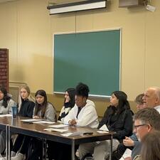 Panel of students sit at table in front of their school staff